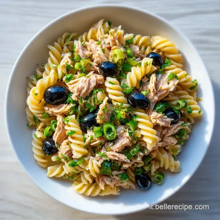 Composizione ordinata di pasta fredda con fiocchi di tonno rosa e olive scure, guarnita con erbe fresche su piatto chiaro.