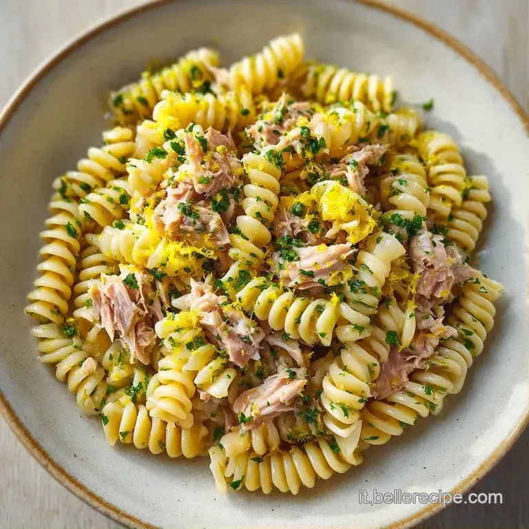 Piatto bianco con pasta cremosa, guarnita da scorza di limone grattugiata gialla e un filo d'olio lucido e trasparente.